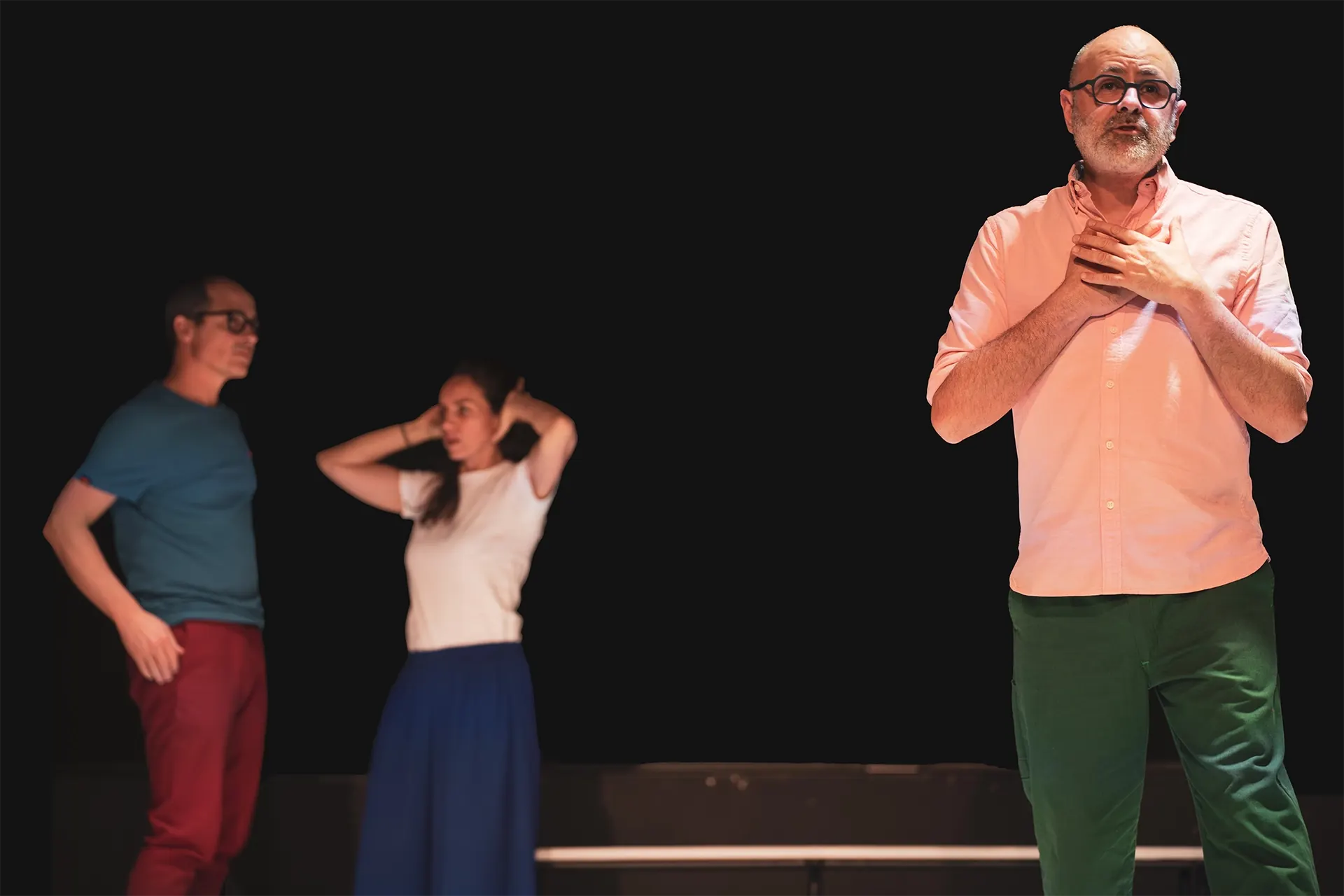 Trois comédiens sur un plateau sombre dans « Scroll » : un homme en chemise rose, une femme et un homme en t-shirt bleu.