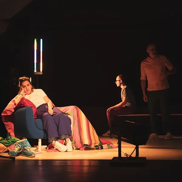 Dans « Scroll », une femme dans un fauteuil bleu sous une couverture rayée ; derrière elle, deux hommes.
