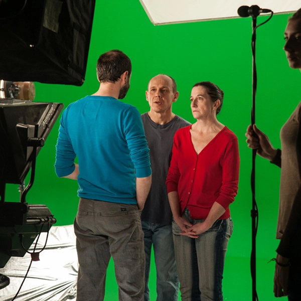 Sur le tournage d’« Easy Coming Out », trois personnes se font face devant un fond vert, un micro perche au premier plan.