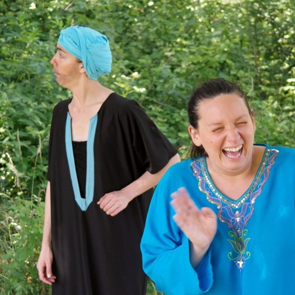 Dans « Ô Grand Nasr Eddin », deux comédiennes en tuniques, l’une en turquoise éclatant de rire, dans la verdure.