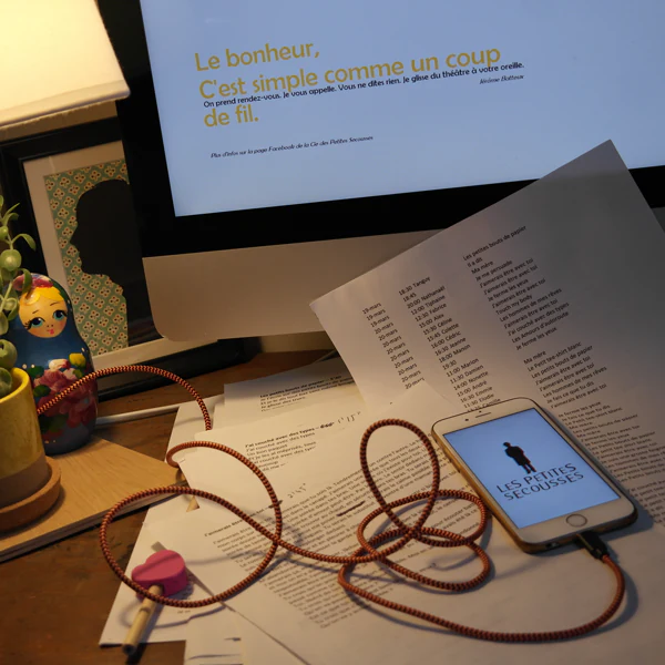 Un smartphone et son câble de casque sur un bureau, devant l’écran « Le bonheur, c’est simple comme un coup de fil ».