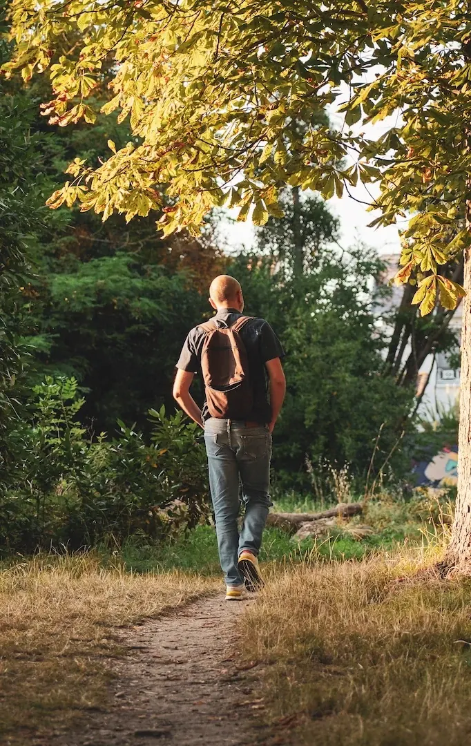 Un homme de dos, sac sur les épaules, marche sur un sentier sous les arbres : « Je me laisse porter » à Talence.