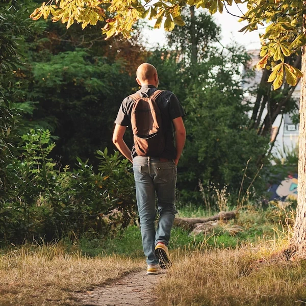 Un homme de dos, sac sur les épaules, marche sur un sentier sous les arbres : « Je me laisse porter » à Talence.